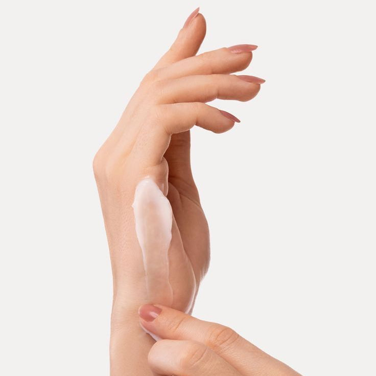 Hand applying a clear cream to another hand against a light background