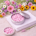 Open tin of pink candies on a white towel with flowers in the background