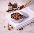 Silver tin filled with chocolate chips on a white towel with coffee beans and extract bottle in the background.